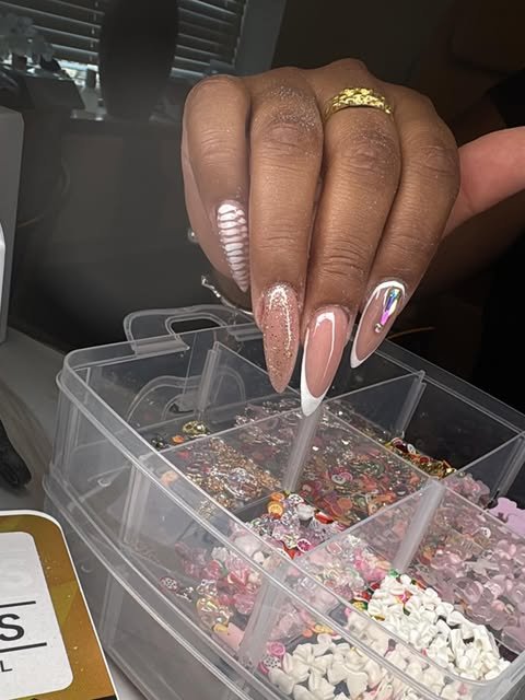 Lange amandelnagels met french tips en glitter boven een doos nail art-steentjes