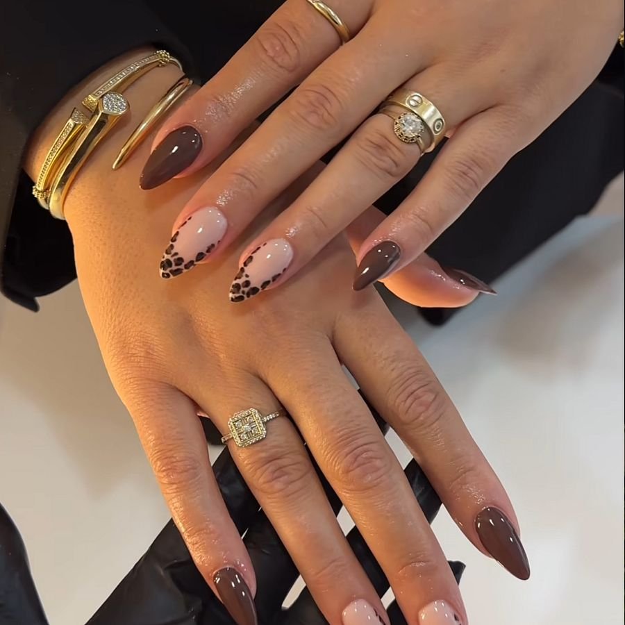 Amandelvormige nagels in nude en chocoladebruin met nail art, gecombineerd met gouden ringen
