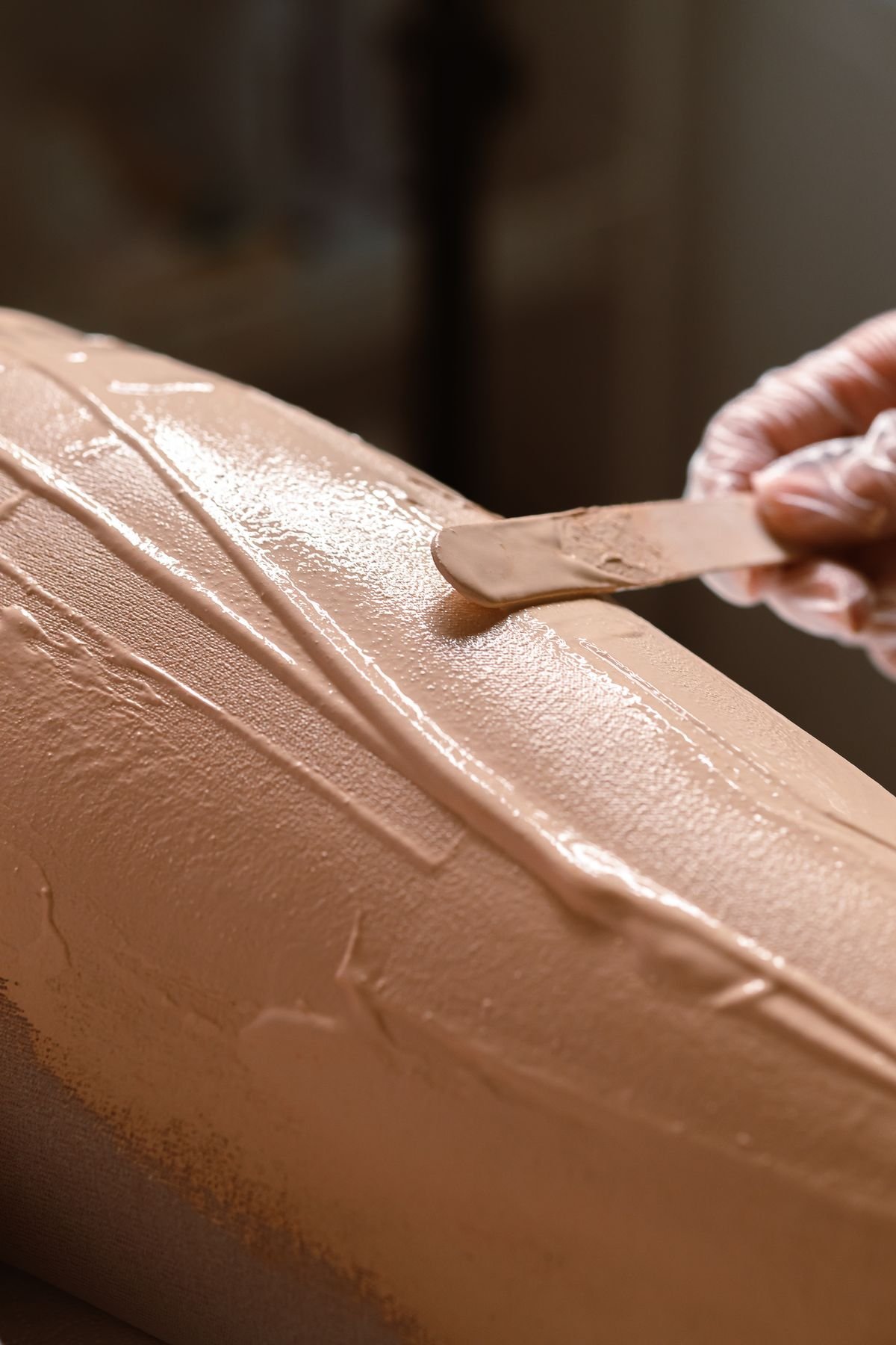 Warme, nudekleurige wax die met een houten spatel op de huid wordt aangebracht